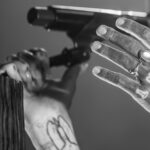 Nightclub scene with a person holding a rifle, focusing on their hand and tattooed arm.