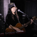 Harper Finn playing guitar and singing at The 13th Floor concert venue.