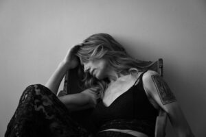 Elegant woman with wavy hair, seated with her head resting on her hand.