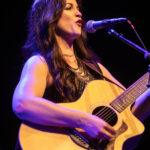 Female musician singing and playing guitar at Deacon Blue concert.